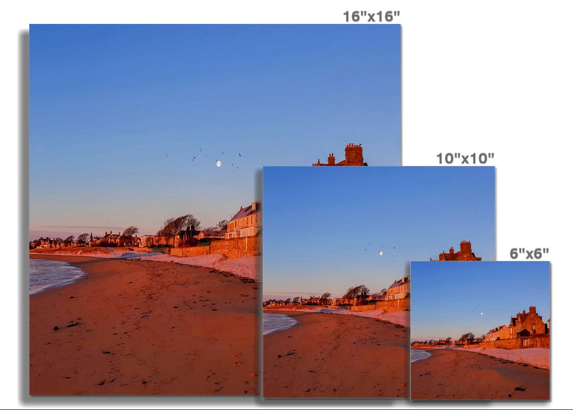 Beach and village edge at Earlsferry, Fife, with houses catching early light and the moon visible, completing a four-image panoramic coastal photograph.
