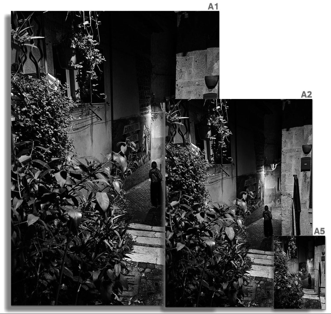 A Mezzanotte black and white fine art photograph of a solitary figure in a narrow Italian street at night